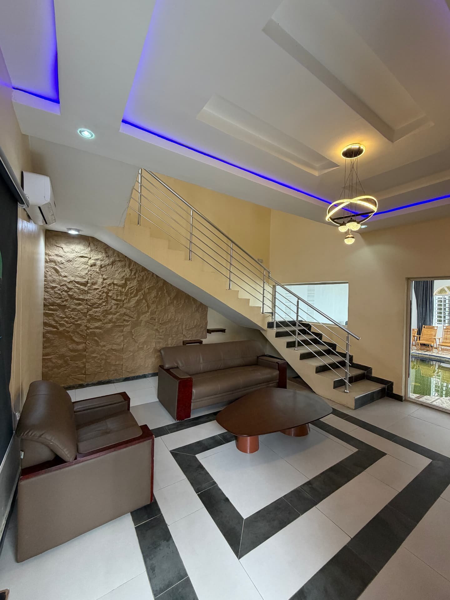 Double-height lounge with leather sofas, stone feature wall and staircase in the 2 Bed pool apartment